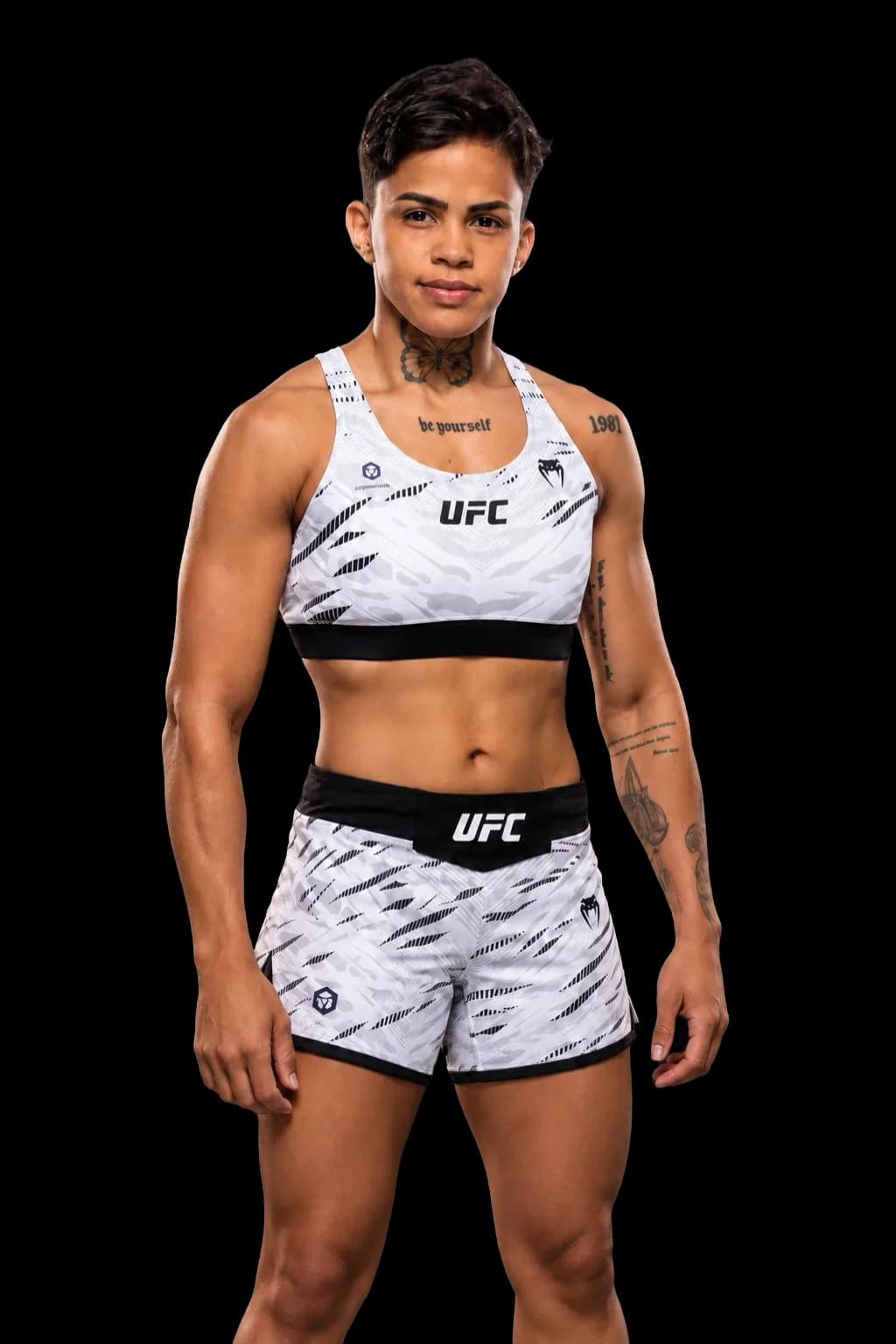 Iasmin Lucindo con conjunto blanco de UFC y tatuajes visibles sobre un fondo gris oscuro.