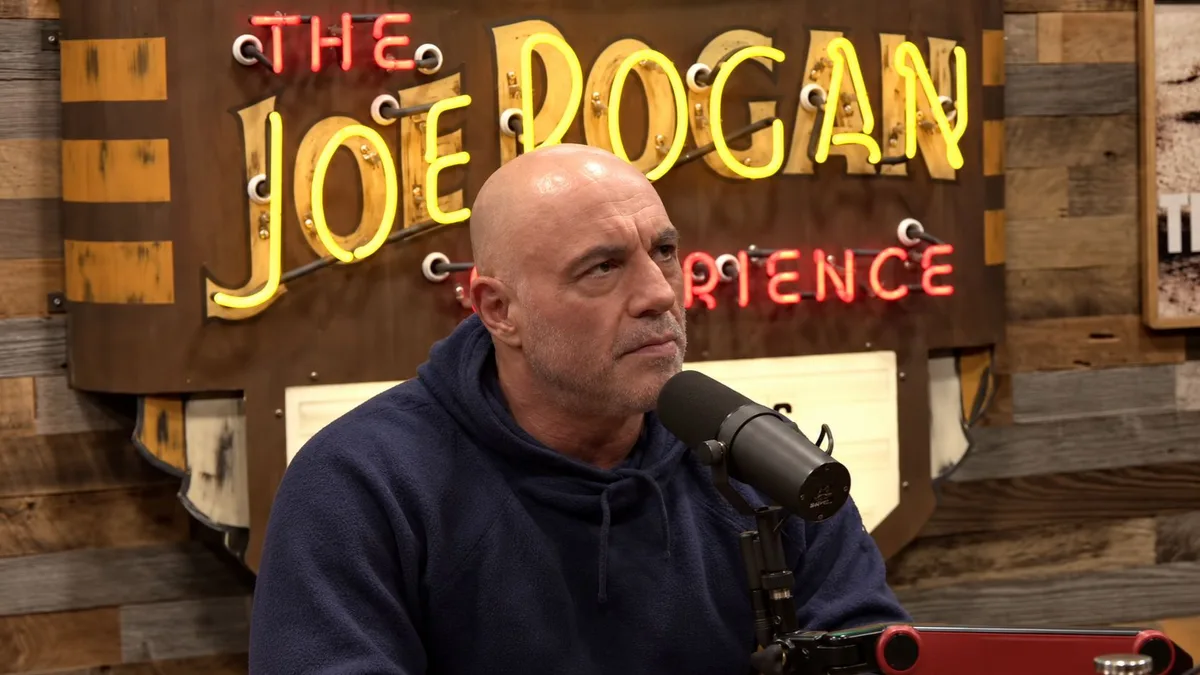 Joe Rogan con expresión seria frente al micrófono en su estudio de pódcast.