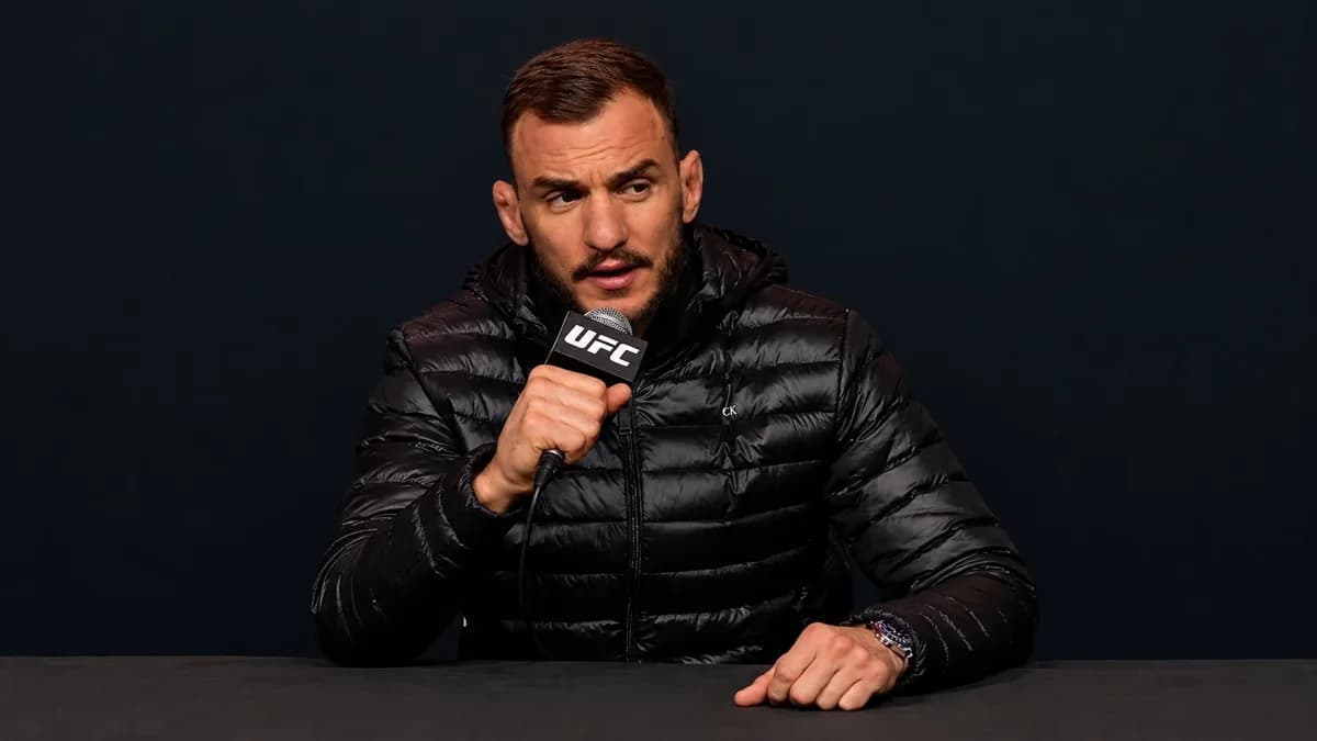 Renato Moicano habla con un micrófono de UFC, vestido con una chaqueta negra durante una conferencia de prensa.