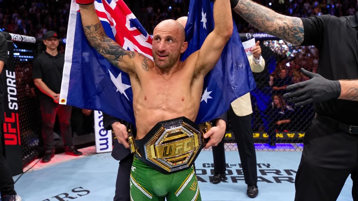 Alexander Volkanovski celebra con los brazos levantados, la bandera australiana y el cinturón de UFC en la cintura.